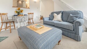 A modern living room with a blue sofa, wooden chairs, a dining table with a floral tablecloth, and a staircase. - 2 Bed in Swimbridge (oc-p44771) (Swimbridge)