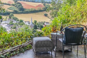A terrace with wicker furniture overlooking a village with a church spire. - 2 Bed in Swimbridge (oc-p44771) (Swimbridge)