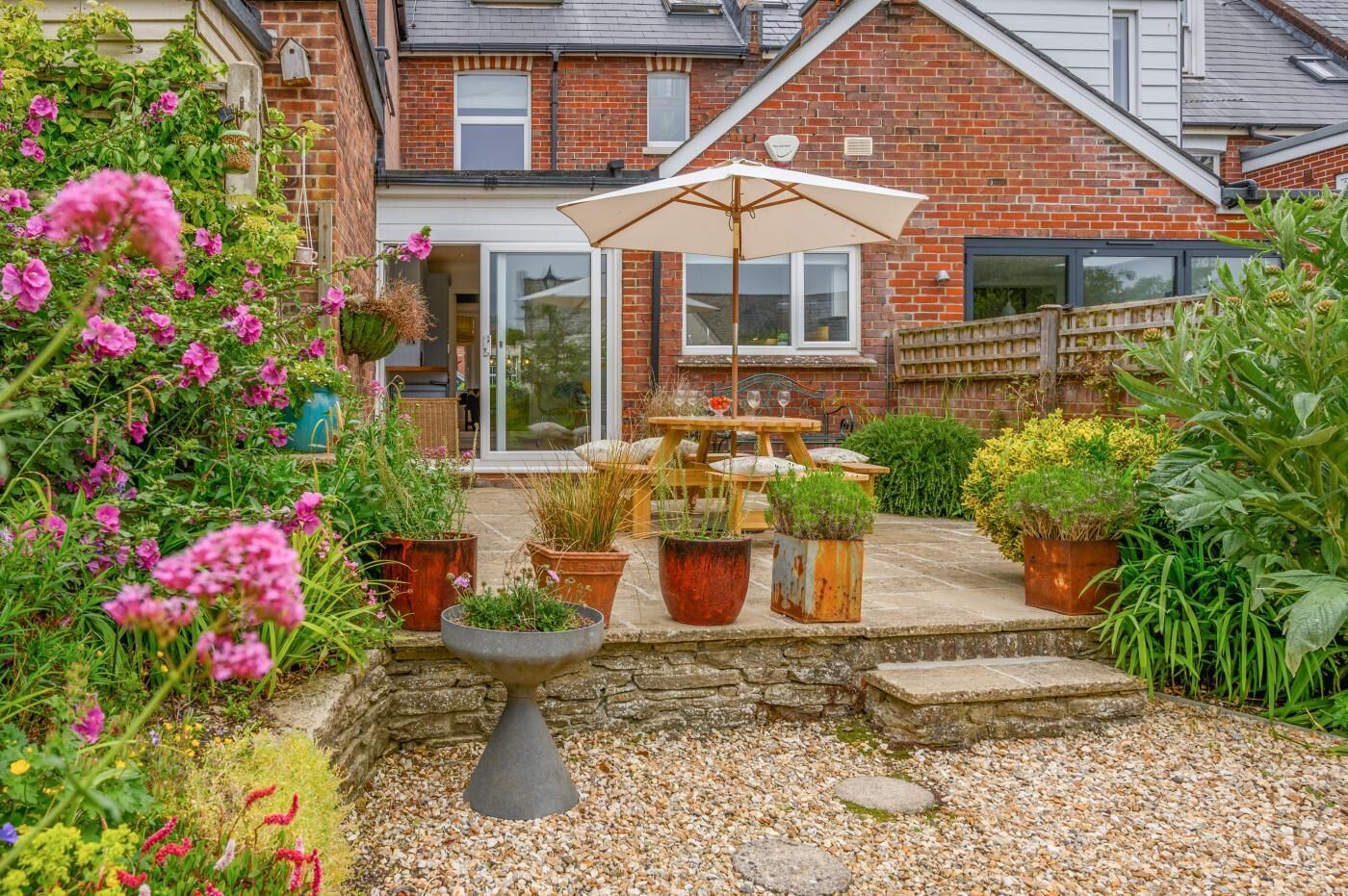A patio with a table and chairs, surrounded by potted plants and a stone fountain.