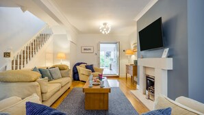 Ein Wohnzimmer mit Sofa, Couchtisch, Kamin, Fernseher und einer Treppe.