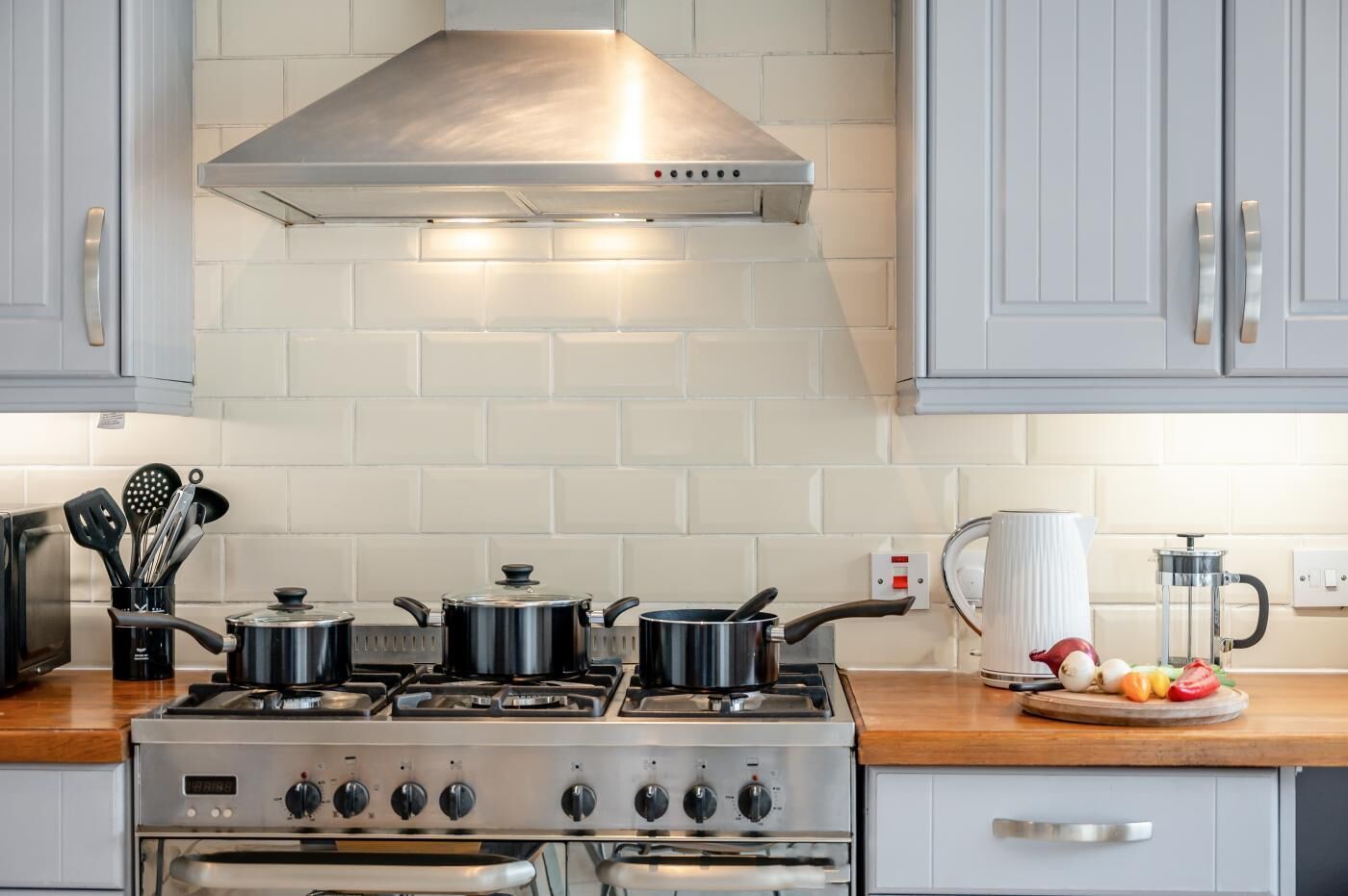 A kitchen with a stainless steel stove, oven, and a range hood. There are pots on the stove, a coffee maker, and a fruit bowl on the counter.