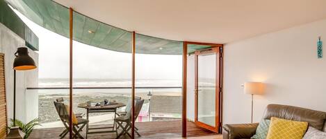 Une pièce dotée d’un plafond incurvé, d’une porte vitrée donnant sur un balcon avec vue sur la mer, d’un canapé en cuir agrémenté de coussins et d’une table avec des chaises.