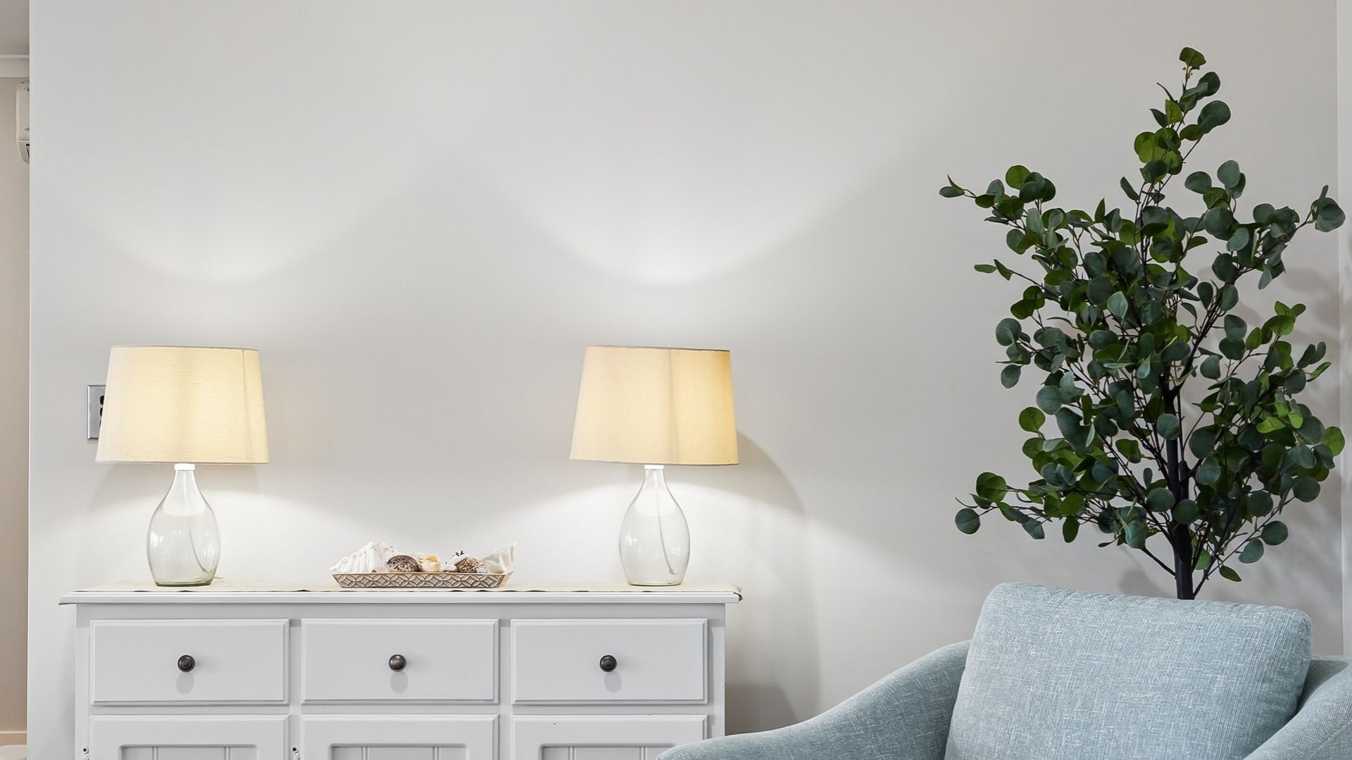 Ein Zimmer mit einem weißen Schminktisch, zwei Lampen, einer Pflanze und einem blauen Stuhl.
