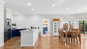 A modern kitchen with a central island, dining area with wooden chairs, and a view of the outdoors.