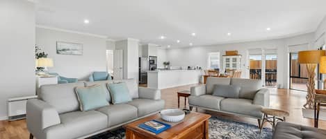 A modern living room with a sofa, coffee table, and a dining area in the background.