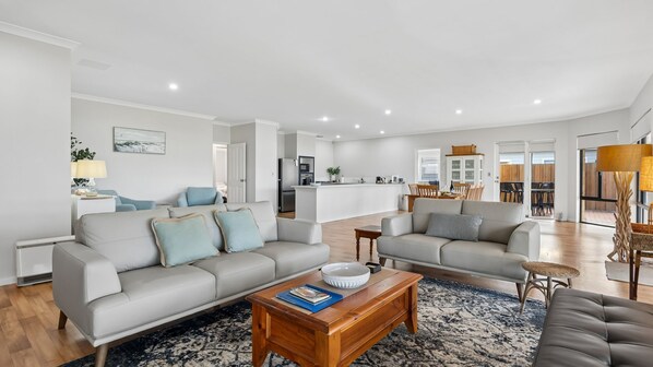 A modern living room with a sofa, coffee table, and a dining area in the background.