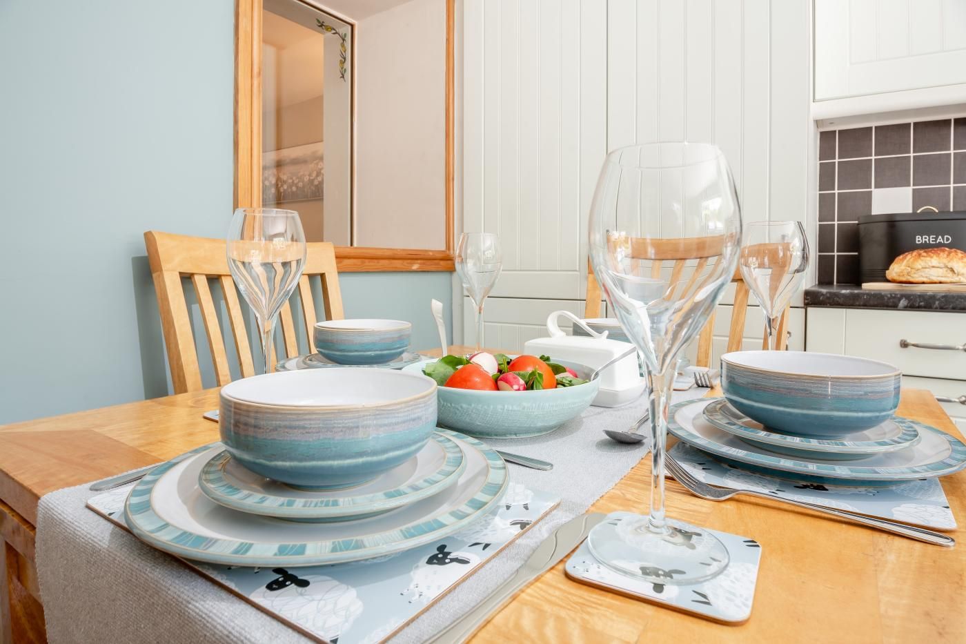 A dining table set with blue plates, bowls, and wine glasses, with a salad and bread on the table.