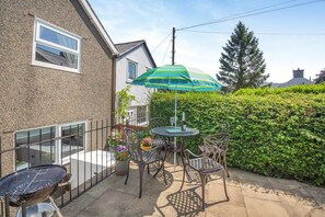 Eine Terrasse im Freien mit Tisch, Stühlen, einem Grill und einem grünen Sonnenschirm.