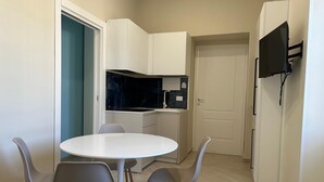 A compact kitchen with a white countertop, a black backsplash, and a white door. There is a round table with four chairs and a flat-screen TV mounted on the wall. - Beautiful 4-bedroom resort with AC in tranquil Pompei (POMPEI)
