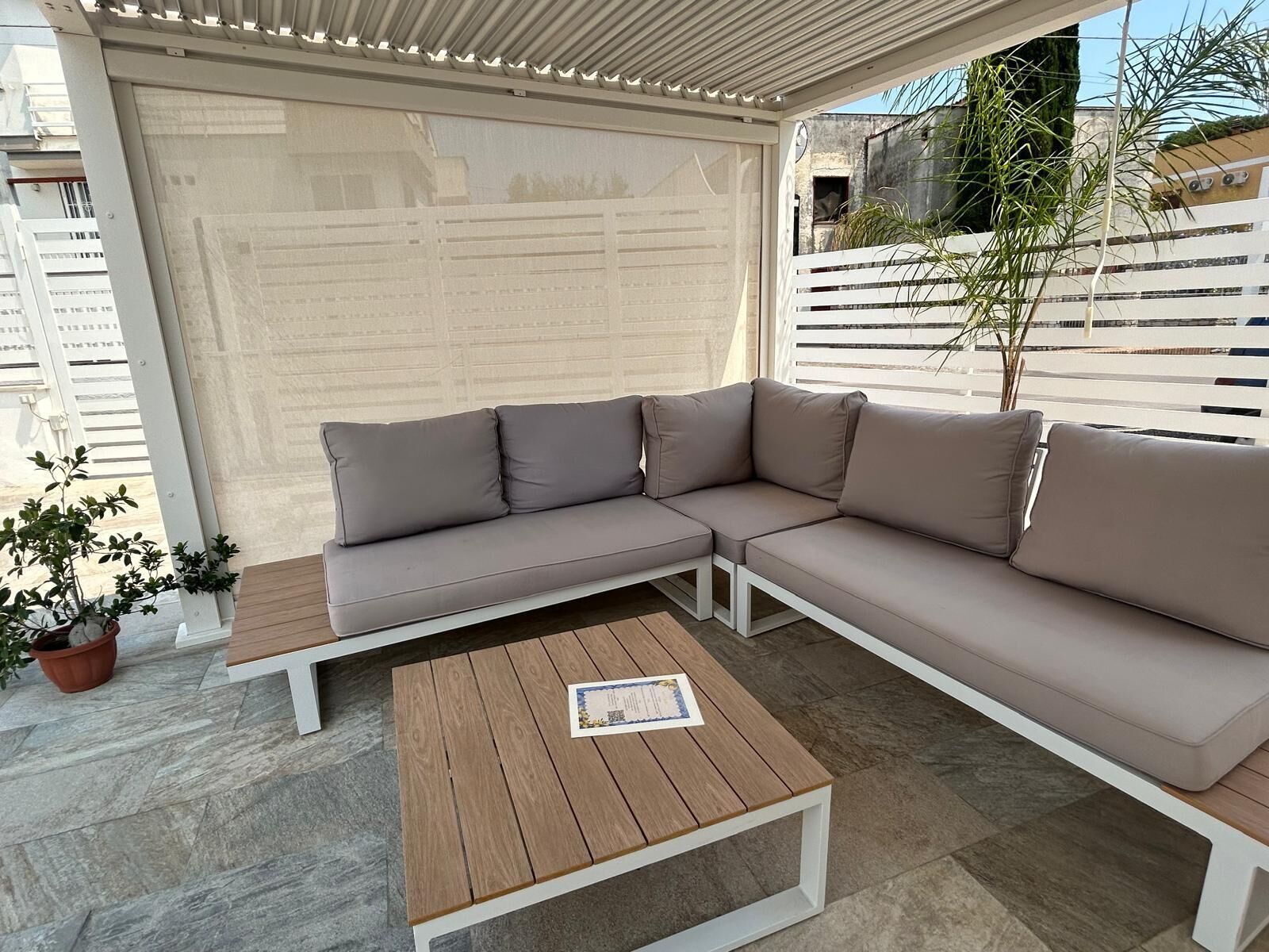 Un espace extérieur aménagé, abrité, avec un canapé d’angle et une table basse en bois.