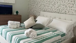 A neatly made bed with striped bedding, a white headboard, and a wall with a leaf pattern. - Beautiful 4-bedroom resort with AC in tranquil Pompei (POMPEI)