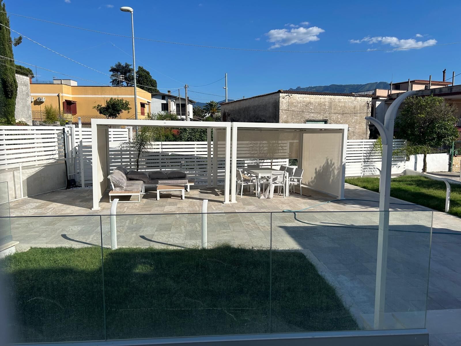 Un espacio de estar techado al aire libre con una mesa y sillas, rodeado por una cerca blanca.
