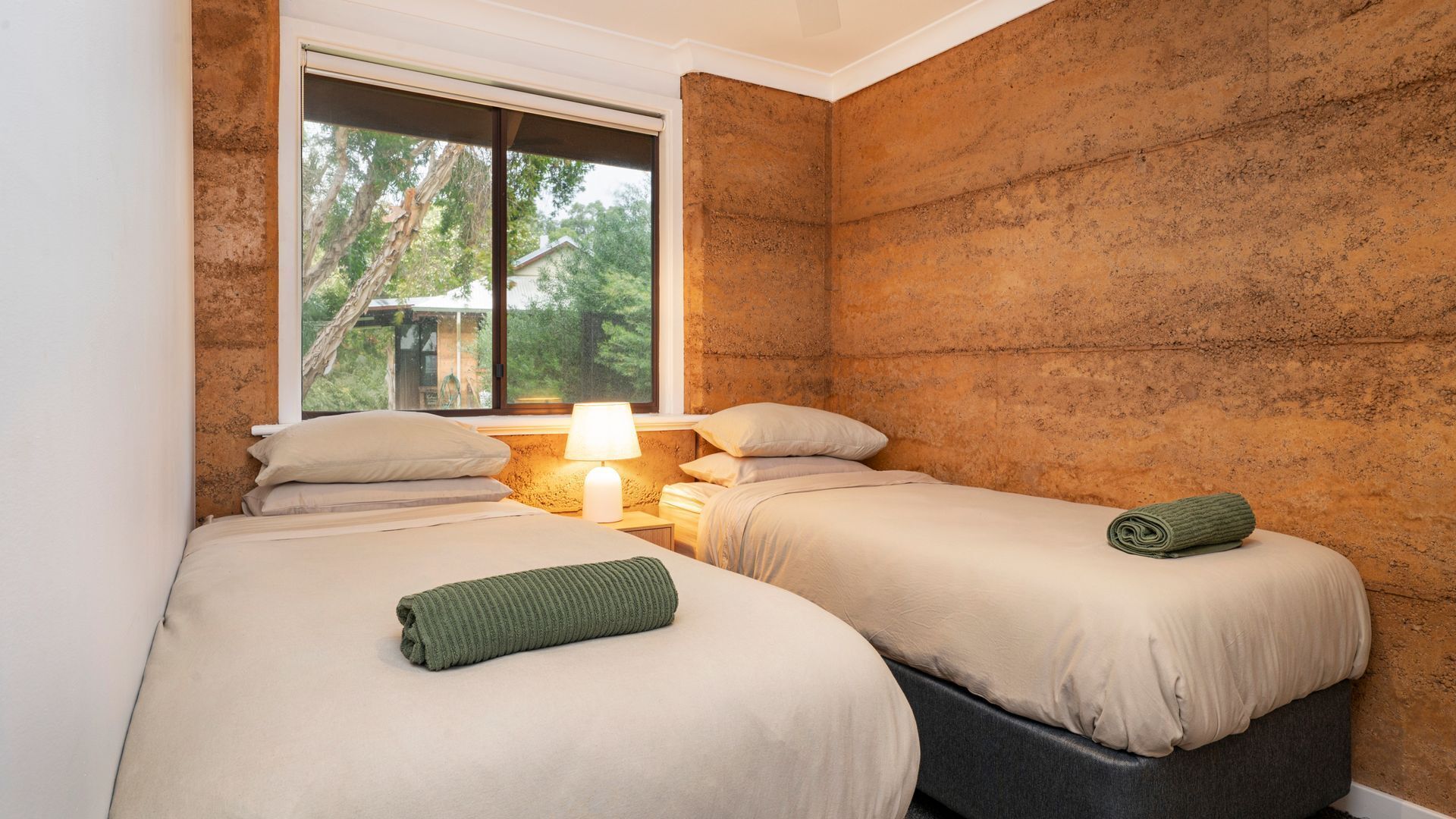 Una habitación con dos camas, una ventana con vistas a árboles y una pared con textura.
