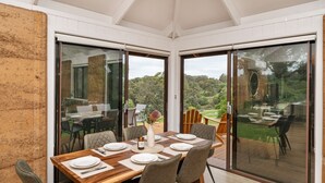 A dining area with a table set for four, large sliding glass doors, and a view of a lush landscape.