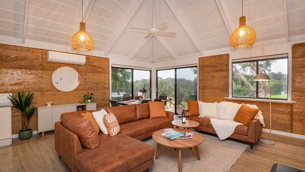 A spacious living area with a large brown sofa, a coffee table, and a dining area with a view of the outdoors.