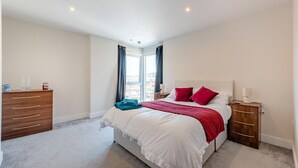 A bedroom with a bed, a wooden dresser, a nightstand, and a window with curtains. - 2 Bed in Maritime Quarter (oc-m44948) (Swansea)