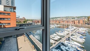 A view from a high-rise window overlooking a marina with boats docked, a clear sky, and buildings in the background. - 2 Bed in Maritime Quarter (oc-m44948) (Swansea)