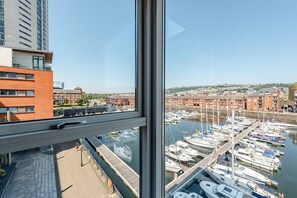 Blick vom Hochhausfenster auf einen Hafen mit vertäuten Booten, wolkenlosem Himmel und Gebäuden im Hintergrund.