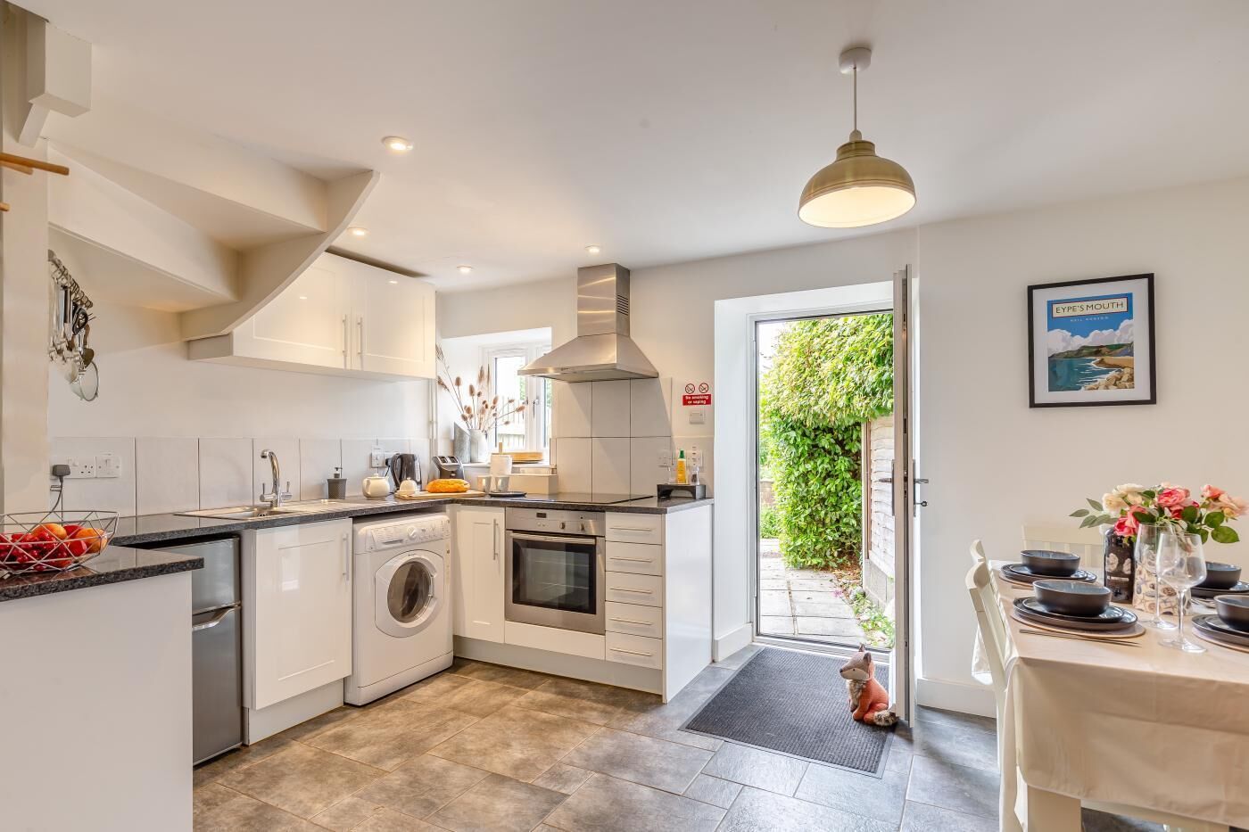 A modern kitchen with a built-in washing machine, oven, and a dining area with a table set for six.