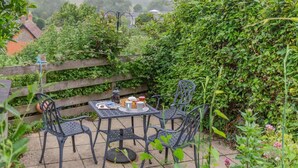 A patio with a table and chairs, surrounded by greenery and a wooden fence. - 2 Bed in Eype (oc-l42804) (Eype)
