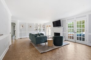 Uma sala de estar ampla, com lareira, televisão e vista para o exterior.