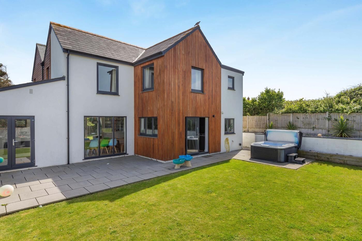 Une maison moderne à deux étages, dotée d’un grand patio, d’un jacuzzi et d’une pelouse bien entretenue.