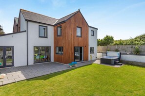 Ein modernes, zweistöckiges Haus mit einer großen Terrasse, einem Whirlpool und einem gepflegten Rasen.