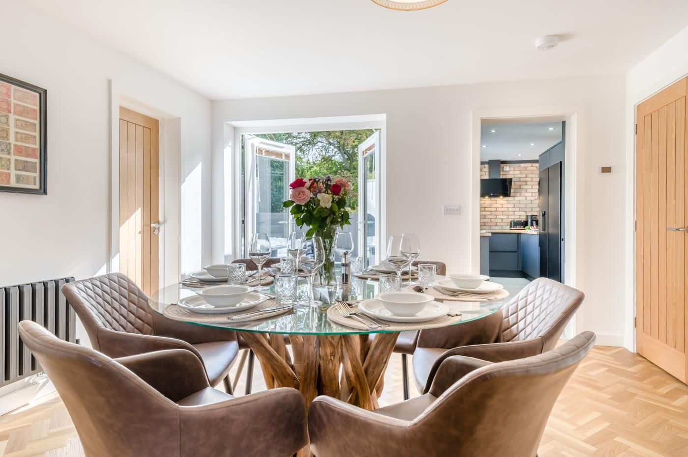 A modern dining area with a glass table surrounded by cushioned chairs, a vase with flowers, and a view of the outdoors.
