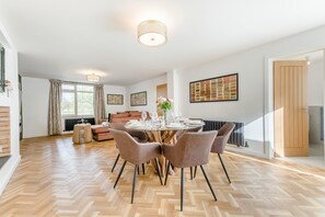Un comedor con una mesa redonda dispuesta para cuatro personas, rodeada de sillas, en una habitación con suelo de espiga y chimenea.