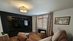 A modern living room with a flat-screen TV, wooden flooring, a sofa set, and a patterned wall. - 4 Bed in Hampeth (oc-w45221) (Shilbottle)