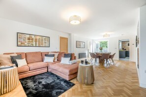 Una sala moderna con un sofá modular, una mesa de comedor con sillas, un tapete negro y un suelo de madera con diseño en espiga.