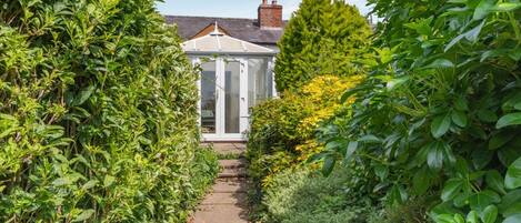 A garden pathway leading to a conservatory with a brick roof and glass doors.