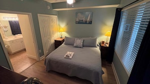 Een slaapkamer met een bed, bedlampen, een plafondventilator, een deur en een raam met jaloezieën.