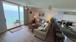 Een woonkamer met een bank, salontafel en een eethoek met stoelen. Er is een balkon met uitzicht op de oceaan.