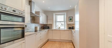 A modern kitchen with built-in ovens, a microwave, and a window with blinds.
