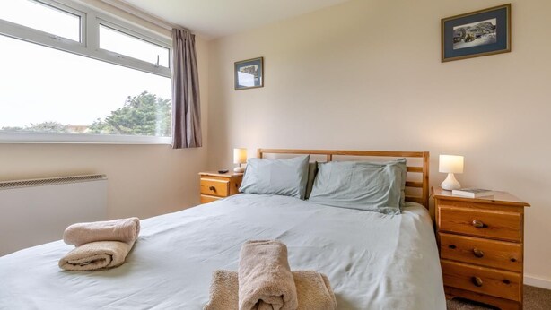A neatly made bed with two towels, a wooden headboard, and two bedside tables with lamps. - 3 Bed in Fairbourne (oc-f42826) (Fairbourne)