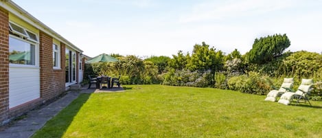 A residential backyard with a patio, a lawn, and a row of white chairs.