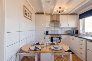 A modern kitchen with white cabinets, a round dining table set for four, and a built-in oven. - 2 Bed in Brixham (oc-k45223) (Brixham)