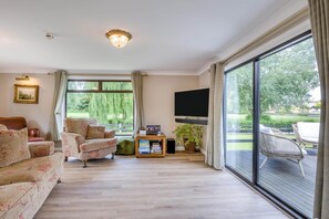 A spacious living room with a large window, a flat-screen TV, and a wooden floor.