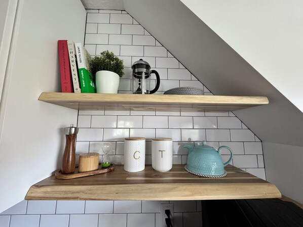 Una cocina con salpicadero de azulejos blancos, estantes de madera y diversos utensilios de cocina.