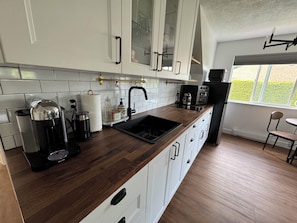 Una cocina con armarios blancos, encimera de madera, un lavabo negro, una cafetera y un tostador.