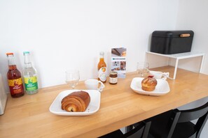 A wooden table with croissants, a bottle of beer, a bottle of water, and a glass. - Le Verdun - Appartement cosy proche Croix-Rousse (Caluire-et-Cuire)
