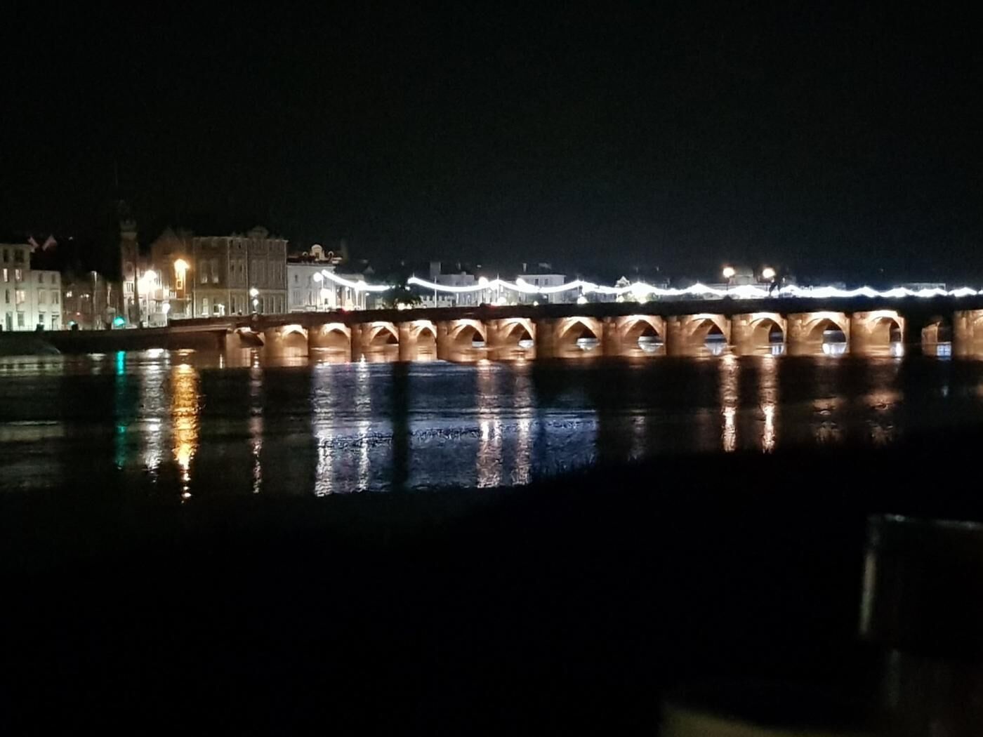 A nighttime view of a bridge with illuminated arches over a body of water, reflecting lights.