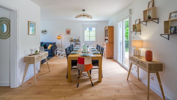 Uma área de refeições com mesa de madeira, cadeiras e vista para o exterior.