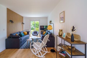 A modern living room with a sofa, a rocking chair, a coffee table, and a TV. - L'Escapade Bretonne - À 2 km de la plage (Fouesnant)