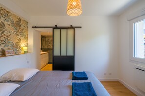A bedroom with a bed, a sliding door to a bathroom, a window, and a wall with a floral pattern. - L'Escapade Bretonne - À 2 km de la plage (Fouesnant)