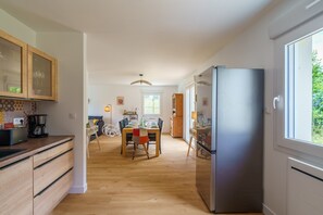 A modern kitchen with wooden cabinets, a dining area with a table and chairs, and a large refrigerator. - L'Escapade Bretonne - À 2 km de la plage (Fouesnant)