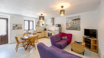 A modern living room with a purple sofa, wooden dining table, and a kitchen in the background.