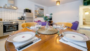 A dining table set with plates, cutlery, and glasses, surrounded by chairs, in a modern kitchen with appliances and a painting on the wall. - L’Escapade Lanvollonnaise - Plage à 15 min (Lanvollon)