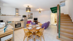 A modern kitchen with a dining area, a staircase, and a living room with a sofa. - L’Escapade Lanvollonnaise - Plage à 15 min (Lanvollon)